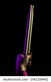 Child Hand Hold Wooden Drum Sticks On Black Backlit Violet-Coloured Background. Rock Music Concept. Unrecognizable. Soft Focus