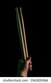 Child Hand Hold Wooden Drum Sticks On Black Backlit Green Background. Rock Music Concept. Unrecognizable. Soft Focus