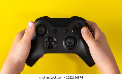 Child Hand Holding Black Game Controller On Yellow Background