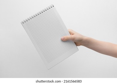 Child Hand Holding Blank Notebook Above A White And Gray Background, Copy Space