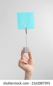 Child Hand Holding Blue Blank Reminder Or Paper Notes Above A White And Gray Background, Copy Space