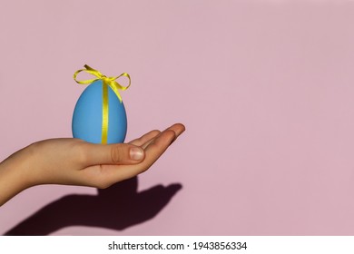 Child Hand holding blue painted easter egg decorated with a yellow bow. Happy Easter concept.