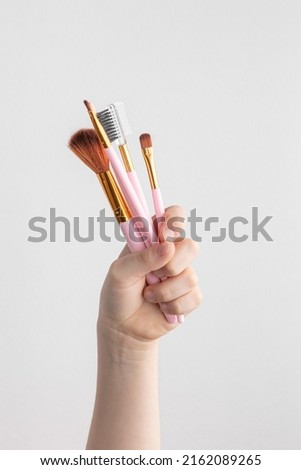child hand holding many pink makeup brushes above a white and gray paper background, copy space