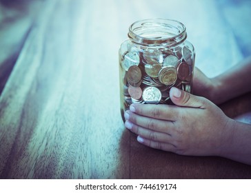 Child Hand Holding  Money Coin Jar On Wooden Table With Window Light, Saving Money Concept