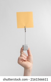 Child Hand Holding Orange Blank Reminder Or Paper Notes Above A White And Gray Background, Copy Space