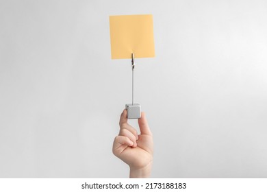 Child Hand Holding Orange Blank Reminder Or Paper Notes Above A White And Gray Background, Copy Space