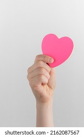 child hand holding pink blank reminder or paper notes in the shape of a heart above a white and gray background, copy space