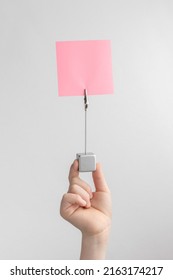 Child Hand Holding Pink Blank Reminder Or Paper Notes Above A White And Gray Background, Copy Space