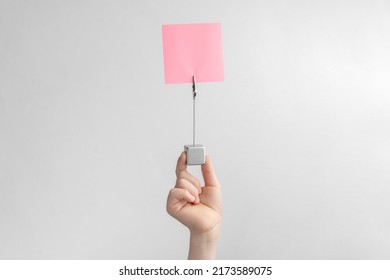 Child Hand Holding Pink Blank Reminder Or Paper Notes Above A White And Gray Background, Copy Space