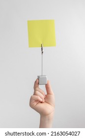 Child Hand Holding Yellow Blank Reminder Or Paper Notes Above A White And Gray Background, Copy Space