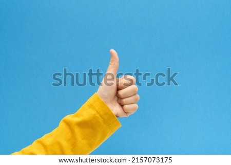 Child hand making thumb up gesture on bright blue background.