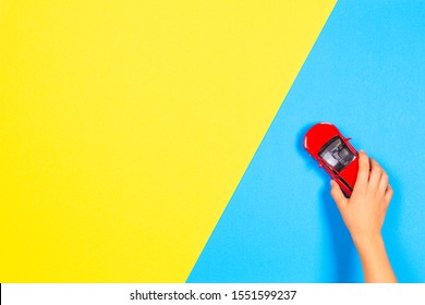 Child Hand Playing Red Toy Car On Light Blue And Yellow Background