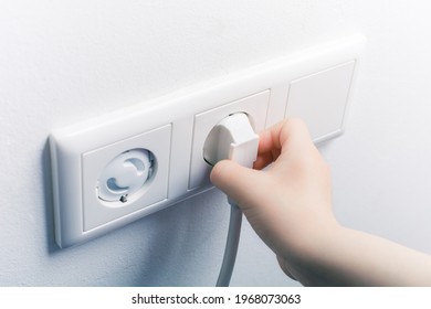 Child Hand Pulling A Power Cord Out Of A Wall Socket With Safety Plugs - Prevent Child Hazard Concept