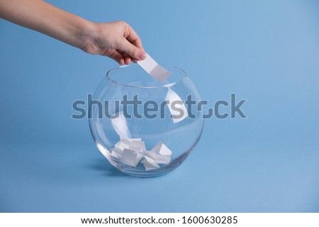 Child hand randomly picking a paper from a glass bowl, random name ballot, simple raffle. Secret Santa 