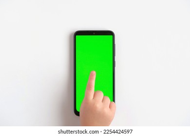 Child hand touching clicking on mobile phone with chromakey screen. Little Baby Finger Taps in the center of blank phone green display. Close up. Using smartphone device. Top view Flat lay - Powered by Shutterstock