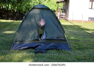 Child Hand Waving Hello Or Hi From Closed Small Tent On Lawn Green Grass In Backyard. Outdoor Recreation, Camping Concept.
