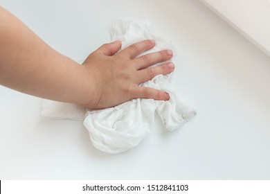 Child hand and white rag cleaning windowsill from dust.