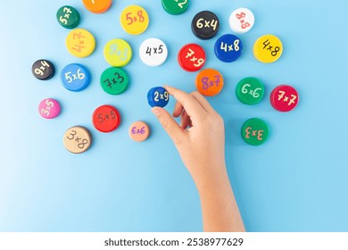 Child hands arranging colorful bottle caps with multiplication problems on a blue background. Flat lay educational concept for learning and math games, Times Tables. tables learning resources - Powered by Shutterstock