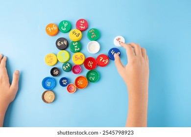 Child hands arranging colorful bottle caps with multiplication problems on blue background, flat lay educational concept for kids, learning math through games, multiplication table activity,  - Powered by Shutterstock