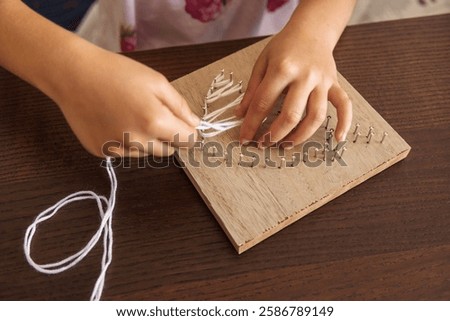 Child hands creating string art on wood. Developing fine motor skills, patience, and creativity.