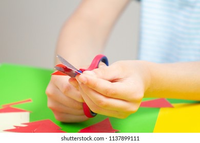 Child Hands Cutting Colored Paper With Scissors At The Table