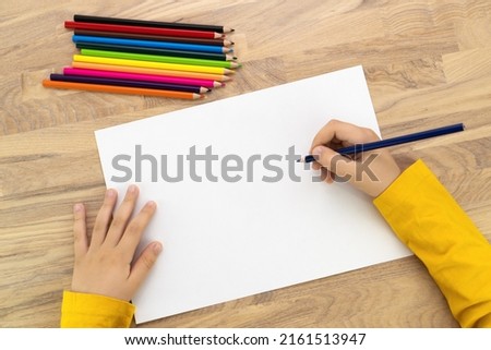 Child hands drawing with pencil on white paper, top view. Kids painting mock up.