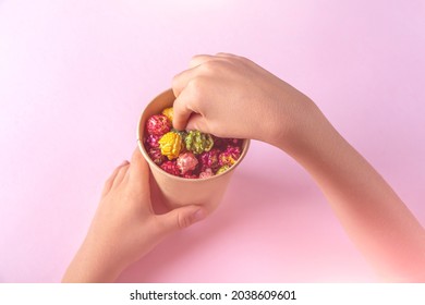 Child Hands Holding Box With Colorful Rainbow Caramel Candy Popcorn On Pink Background. Cinema Snack Concept. Watching Movie And Entertainment. Flat Lay. 