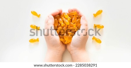 Child hands holding fish oil capsules on white background. Omega 3, fish fat capsules in kid's hands. Children's health care concept.