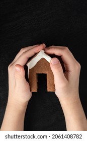 Child Hands Holding Gingerbread House. Top View, Black Background.