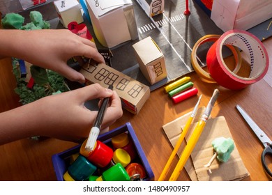 Child hands making paper city mockup with restaurant, gym, church, hotel and tour bus Welcome.