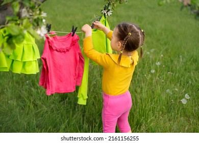 Child hanging wet clothes after laundry on a clothesline with clothespins outdoors in the garden. Drying after washing. Washing colored clothes with safe detergents for laundering colors stuff
