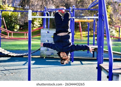A child hangs upside down on playground equipment.