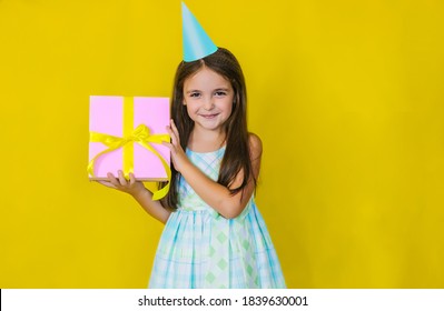 The child has a happy face holding a gift box on a yellow background.The girl has long hair,a charming happy face celebrating her birthday. The kid is happy, loves birthday and holidays.