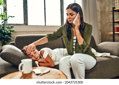 The child has a high fever. Mom touches her daughter's forehead and calls an ambulance. The little girl got sick. - Powered by Shutterstock