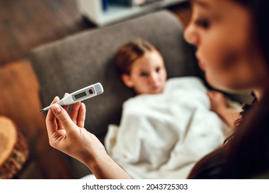 The child has a high fever. Mom looks at the thermometer, measures her daughter's temperature.