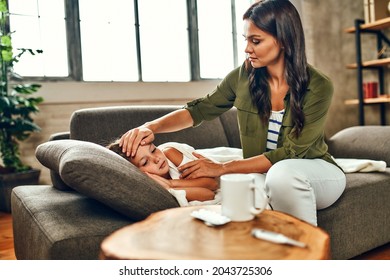 The Child Has A High Fever. Mom Touches The Forehead Of Her Daughter, Who Is Lying Under The Covers On The Couch And Is Sick.