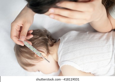 Child Has A High Temperature Or Fever. Sad Mother Measures The Temperature Of Baby Using A Thermometer. Closeup. Flu. 