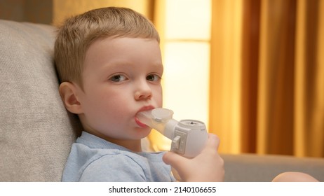 Child Has Respiratory Infection Or Bronchitis, And He Is Breathing Heavily. Blond Caucasian Child With Asthma Problems Inhales With Tube In His Mouth. Treatment Of Pneumonia With Nebulizer At Home.