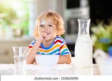 Child Having Breakfast. Kid Drinking Milk And Eating Cereal With Fruit. Little Boy At White Dining Table In Kitchen At Window. Kids Eat On Sunny Morning. Healthy Balanced Nutrition For Young Kids.