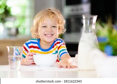 Child Having Breakfast. Kid Drinking Milk And Eating Cereal With Fruit. Little Boy At White Dining Table In Kitchen At Window. Kids Eat On Sunny Morning. Healthy Balanced Nutrition For Young Kids.