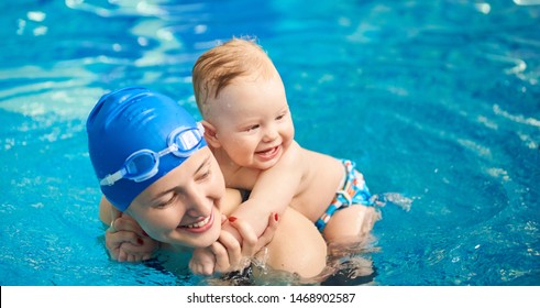 Child having fun in water with mom. Little wet boy smiling holding on his mother's back and happy woman with swimming cap and goggles. Blue turquoise water on background. Horizontal portrait view
