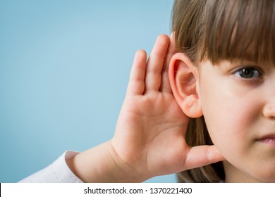 Child with hearing problem on blue background. Hearing loss in childhood, symptoms and treatment concept. Close up, copy space.