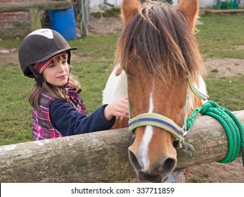 Child with helmet stroking pony on a farm