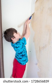 A child helps remove old wallpaper from a wall as the first step in redecorating.