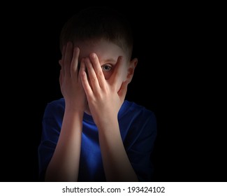 A Child Is Hiding His Eyes In The Dark And Looks Scared Or Upset. The Boy Is Isolated On A Black Background For A Fear Or Sadness Concept.