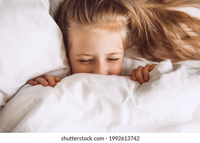 Child Hiding Under Duvet In Bed. Indulge In The Bedroom In The Morning. The Girl Closed Her Eyes Under The Covers Selective Focus