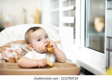 A Child In A High Chair Eating A Cracker With Raisins