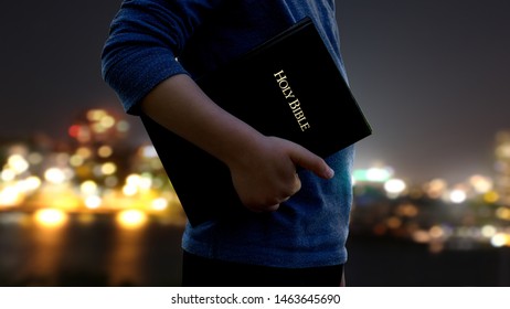 Child Holding Bible In Front Of Chity Lights