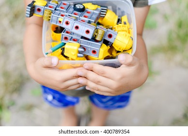 Child Holding Box With Toys On Outdoors Background. Closeup On Hands