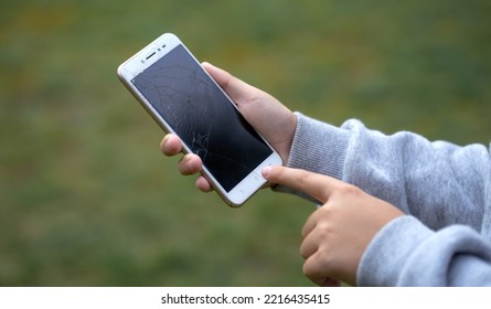 The Child Is Holding A Broken Smartphone In His Hands. Mobile Phone Breakdown, Cracks On The Display. Buying A New Phone To Replace A Damaged One.